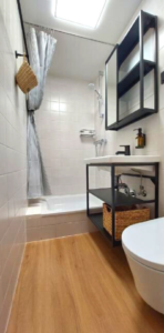 View into bathroom with white tiled walls and a wooden floor, a shower, basin, and toilet.