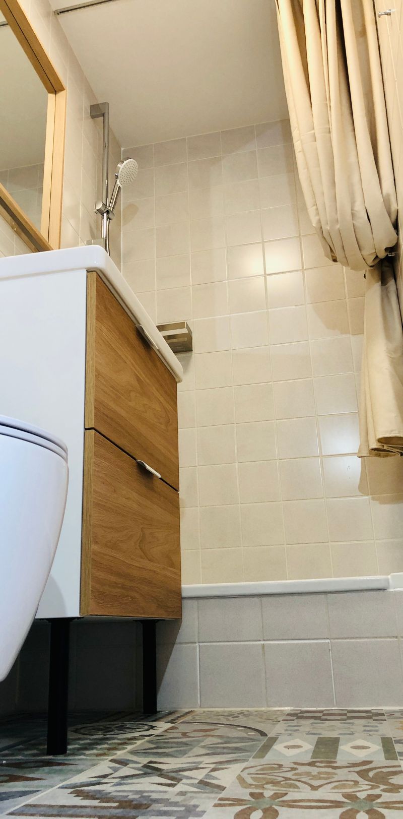 View into bathroom with white tiled walls and a wooden floor, a shower, basin, and toilet. 